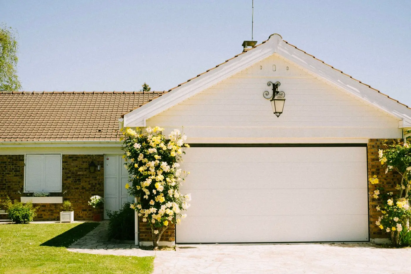 A single-car garage door on a brick house with roses beside it